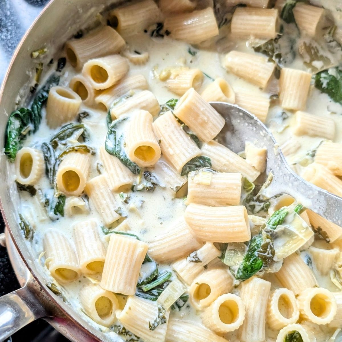 a big pan of creamy spinach artichoke pasta with alfredo sauce and parmesan cheese and cream cheese